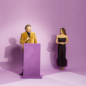 Bryan Cranston, wearing a brown suit, speaks at the Hollywood Awards ceremony. Jennifer Garner, in a black dress, stands attentively next to him.