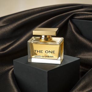 Golden casket holding 'The One' perfume from Dolce & Gabbana. Emblazoned with the brand logo. Displayed on a sleek, black velvet pedestal.