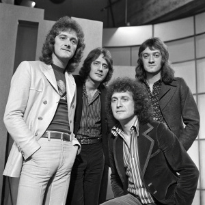 Black and white photograph from 1977. Slade band members: Noddy Holder, Don Powell, Jim Lea, and Dave Hill posing at BBC Pebble Mill TV studio in Birmingham.