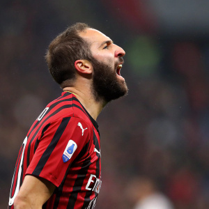Soccer star Gonzalo Higuain, beard, intense look. Striped jersey, red and black. Dynamic pose, blurred stadium crowd background.