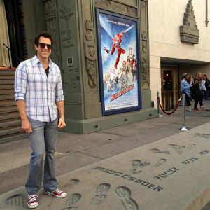 Johnny Knoxville at the TCL Chinese Theatre. Casual outfit, playful smile, standing in front of 'Blades of Glory' movie poster. Outdoor setting with people in background.