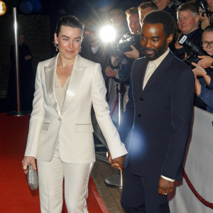 Olivia Williams and Rhashan Stone at the annual film gala. Wearing elegant white and dark suits respectively. Surrounded by fans and paparazzi on the red carpet.