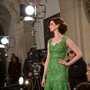 Anna Hathaway on the set of 'The Devil Wears Prada'. Wearing a green dress with intricate lace patterns. Studio lights, cameras, and crew members in the background.