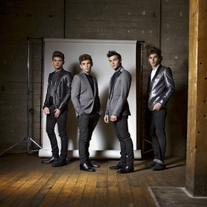 Josh Cuthbert, Jaymi Hensley, JJ Hamblett, and George Shelley of Union J, in sleek black suits, stand out against a stark white backdrop.