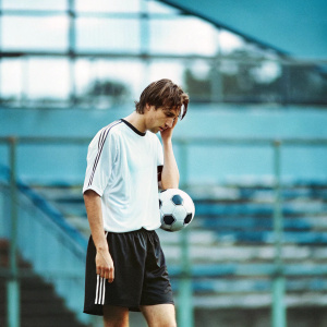 Marco Reus, soccer player, in deep thought. Dressed in Borussia Dortmund's jersey and shorts. On a soccer field, background blurred.