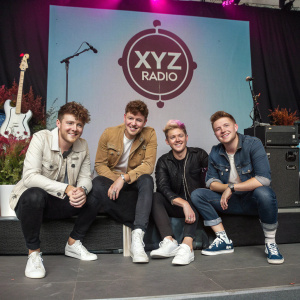 Rixton band members posing in casual wear. Concert stage backdrop featuring XYZ radio logo.