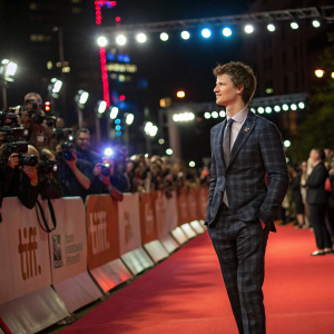 Ansel Elgort at film festival. Wearing a tailored suit. Red carpet scene with flashing cameras and enthusiastic fans