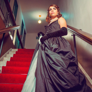 Billie Piper at premiere event, serious look, wearing elegant black dress with long train, pearl necklace, red carpet