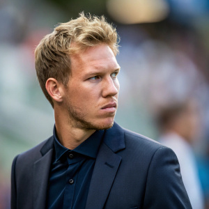 Close-up shot of Julian Nagelsmann, a serious look on his face. The blurred background highlights his sharp suit and styled blonde hair.