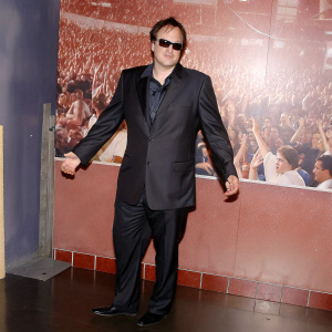 Quentin Tarantino at the Hollywood Walk of Fame. Wearing a black suit and sunglasses, standing in front of a bustling crowd.