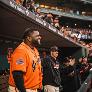 Pablo Sandoval in the dugout, wearing a bright orange team jersey. A crowd of fans cheering in the background.