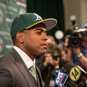 Yoenis Cespedes at a press conference. Serious expression, baseball cap, and formal attire.