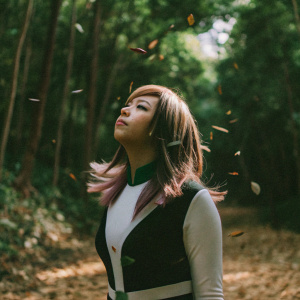 Ochaco Uraraka from My Hero Academia, without helmet, standing in a forest with falling leaves.