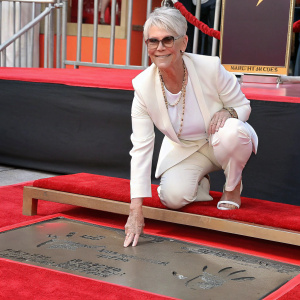 Jamie Lee Curtis, Caucasian actress, posing for a picture with hands imprinted in cement outside the TCL Chinese Theatre. She wears a white blazer and a gold necklace.