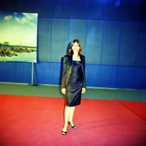 Emily Mortimer, a British actress, at the Shutter Island film premiere. Dressed in a sleek black dress and a matching blazer. Warm smile. Indoor setting with a red carpet and a backdrop featuring the Shutter Island movie poster. Glamorous atmosphere.
