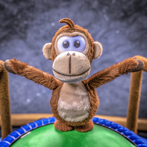 A 3D render of a Diddy Kong inspired character, light brown and soft looking. Cartoonish friendly face, arms spread wide. Dark grey backdrop