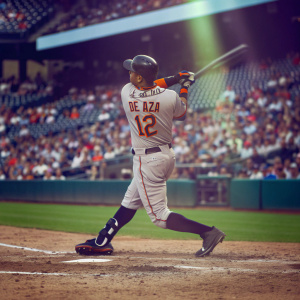 Alejandro De Aza swinging at the ball in a packed stadium. Gray and orange uniform with number 12. Quick snapshot captures the intensity of the moment.