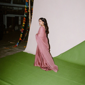 Ileana D'Cruz, draped in a deep red saree, poses elegantly on the set of a Bollywood film premiere. The backdrop is a vibrant, bustling street festival with colorful lights and decorations.