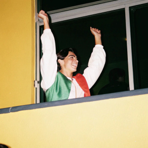 Cristiano Ronaldo in a candid photo, dressed in vibrant green and red jersey. He's celebrating with arms raised, against a blurred stadium crowd background.
