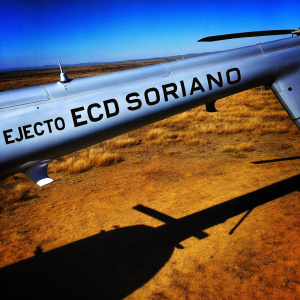 Aerial view of a gray helicopter with 'EJECTO ECD SORIANO' text on its side. Shot from below, highlighting its profile.