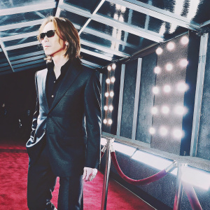 Yoshiki, Asian musician, in black suit and dark shirt, without sunglasses. Standing solo on the Grammy Awards red carpet.