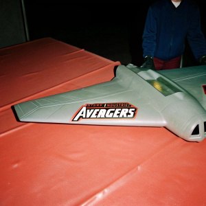 Conceptual design of the Stark Industries Quinjet, a fictional aircraft from Marvel's Avengers. Sleek, aerodynamic gray body with orange accents. Visible logos for Stark Industries and Avengers. Set against a dark backdrop, highlighting the aircraft's advanced technology and futuristic appearance.