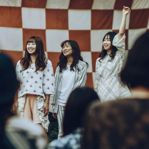 Soyou, Hyorin, Bora, and Dasom of SISTAR at a vibrant fan meet. Casual outfits with colorful patterns. Orange and white checkered backdrop. Even lighting and cheerful expressions.