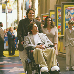 Christopher Reeve, seated in wheelchair, surrounded by family and crowd at the bustling Hollywood Walk of Fame.