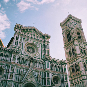 Low angle shot of the Florence Cathedral. Gothic architecture. Tall towers, intricate detailing, white facade, detailed patterns, sculptures. Clear blue sky with wispy clouds.