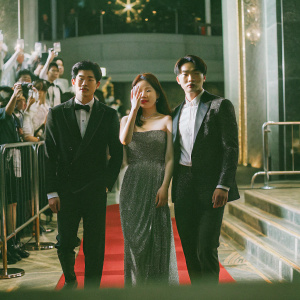 Ok Taec-yeon, Suzy, and Park Jin-young at a glitzy awards show. They are posing for a group photo on a red carpet with flashing cameras.