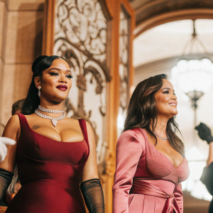 Rihanna and Salma Hayek at a glamorous gala. Rihanna in a deep burgundy gown with a necklace, Salma in a bold pink dress with a fitted waist. Black background with intricate hand-drawn designs.