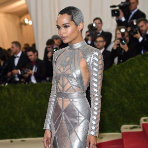 Zoe Kravitz at Met Gala. Wearing an avant-garde silver dress with geometric patterns. Crowded room, flashes of cameras.