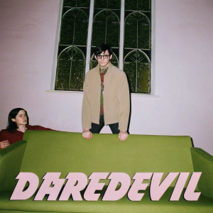 Illustration showcasing the heroes from 'Daredevil': Matt Murdock (Daredevil), Karen Page, Foggy Nelson, Elektra Natchios, and Stick. Matt stands centrally with dramatic facial expression, set against a gothic stained glass backdrop. Muted color palette, comic book style, 'DAREDEVIL' at bottom