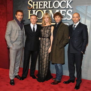 Promotional photo of Robert Downey Jr., Rachel McAdams, Guy Ritchie, Kelly Reilly, and Mark Strong at Sherlock Holmes premiere. Dressed in formal attire, standing in front of red carpet with bold 'SHERLOCK HOLMES' logo backdrop.