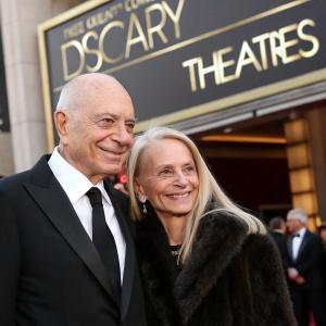 Alan Arkin and Suzanne Newlander Arkin at an Oscar Awards ceremony. Dressed in black suit and elegant fur coat, they smile in front of the Dolby Theatre sign