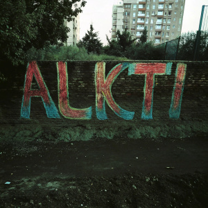 A vibrant mural of the word 'Alkti' painted in bold, swirling colors against a dark urban backdrop.