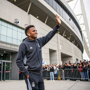 Rodrygo, Brazilian soccer player, outside a stadium. Wearing a casual adidas tracksuit. Smiling and waving to fans.