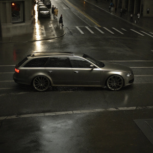 Audi RS6 Avant parked on a rainy city street. Widebody kit, metallic grey, distinctive LED lights, brand name visible