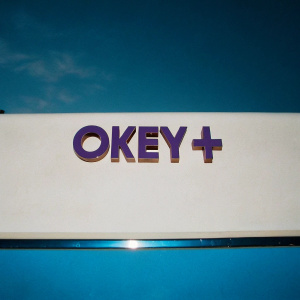 Okey+, sleek logo design. Bold purple text 'Okey+' on pristine white backdrop
