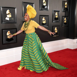 Erykah Badu at Grammy Awards, wearing an extravagant yellow turban and a vibrant green and striped skirt. She beams with joy.