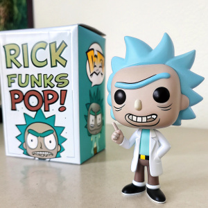A tiny Rick Funko Pop! figurine, playfully posed near its packaging box. The box displays the Pop! vinyl logo alongside Rick and Morty branding.