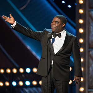 Tracy Morgan, dressed in a black tuxedo, giving an acceptance speech at the Comedy Awards. Applause and flashing lights in the background.