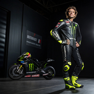 Valentino Rossi, iconic motorbike racer, posing in a sleek racing suit. Sponsor logos prominent. Dynamic pose against dark backdrop, professional setting.