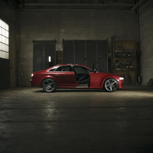 Red Audi RS5 with black trims parked in an open garage. Bright lights highlighting car's design and details.