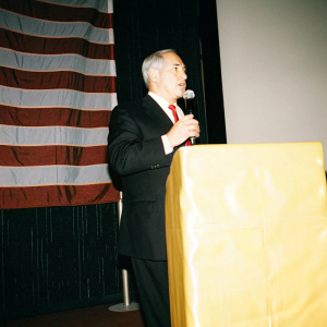 Benjamin Netanyahu, in a dark suit and red tie, giving a speech at UN headquarters. Large American flag as backdrop.