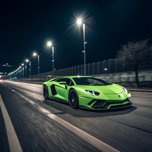 Neon green supercar speeding through empty night street. Lamborghini Aventador's distinctive angular design and brand logo clearly visible