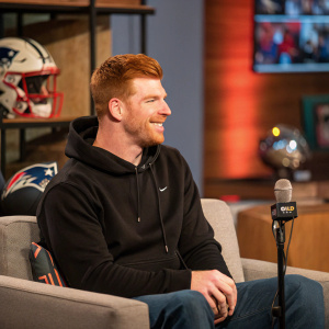 Andy Dalton, in a casual black hoodie, sitting on a couch during a sports interview segment.