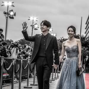 Nathan Lee Seung-hyun and Qi Wei, stars of a K-drama, at the Seoul International Film Festival. Nathan in a black tuxedo, Qi Wei in a stunning blue gown with intricate beadwork. Crowded, illuminated red carpet scene.