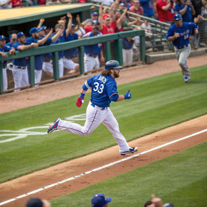 Jarrod Saltalamacchia, wearing a blue jersey with number 33, sprinting across the baseball diamond. Spectators and teammates in the dugout cheer him on.