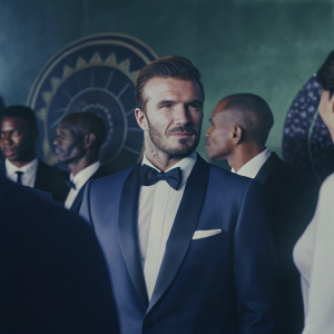 David Beckham in a sleek navy suit with a bow tie, at a crowded gala. Multiple celebrities in formal wear. Dark background with gold and black decorative elements.